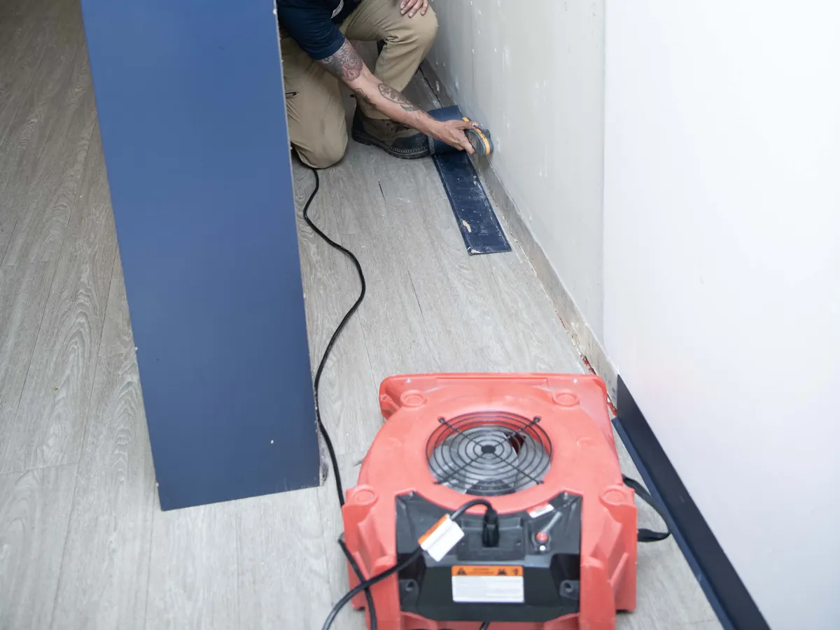Air mover drying a water-damaged wall and floor along a hallway