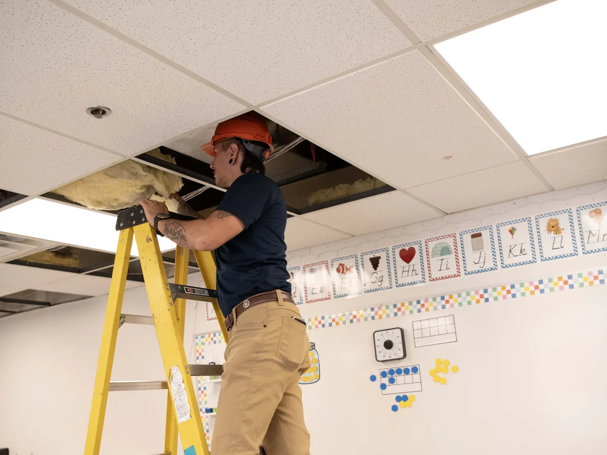 Cavalry technician on a ladder inspecting above a ceiling after a water leak