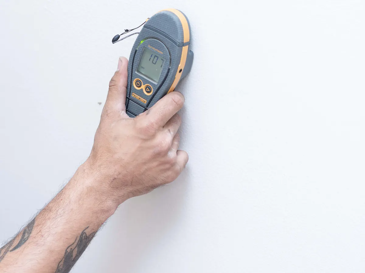 Moisture meter held against drywall to map hidden water